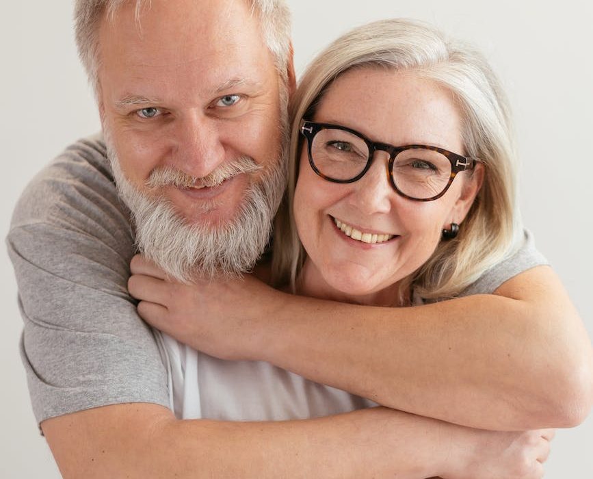 close up shot of a happy elderly couple hugging while looking at camera